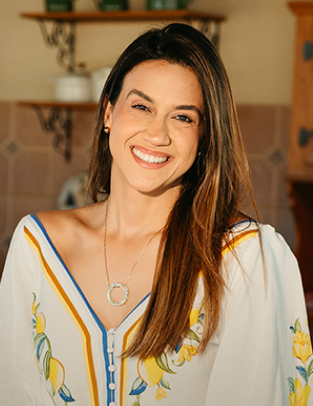 Kellen Pires sorrindo, de blusa branca bordada, em uma cozinha